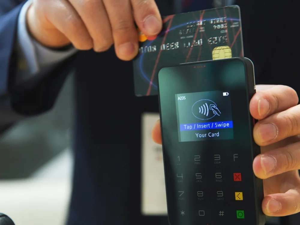 Mastercard credit card with EMV chip held over a contactless reader showing 'Tap / Insert / Swipe Your Card'