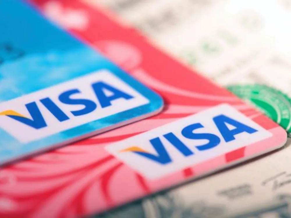 Two colorful Visa credit cards closeup with US dollar bills visible in the background